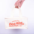 Hand holding a white cool bag with 'Dog Yog' branding on a plain background